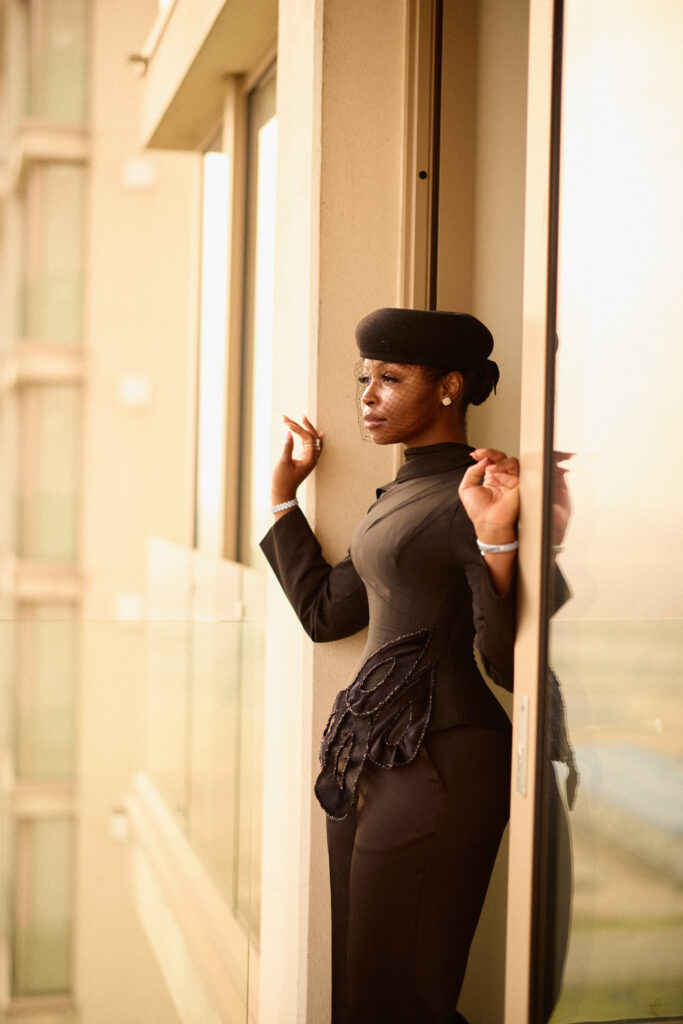 Side view of Sandrah Tubobereni standing in quiet reflection, wearing her tailored black TUBO graduation look and beret.